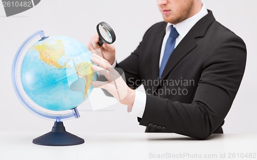 Image of businessman hand holding magnifier over globe