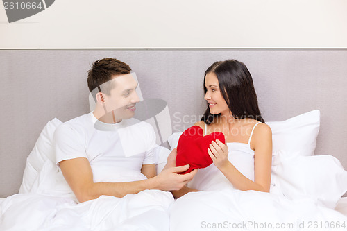 Image of smiling couple in bed with red heart shape pillow