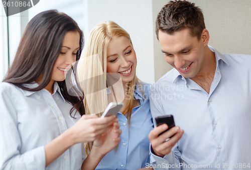 Image of smiling business team with smartphones in office