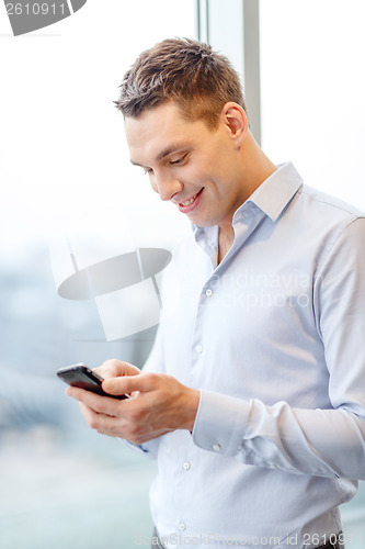Image of smiling businessman with smartphone in office