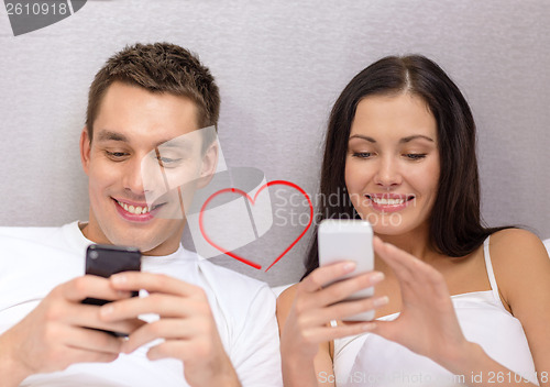 Image of smiling couple in bed with smartphones