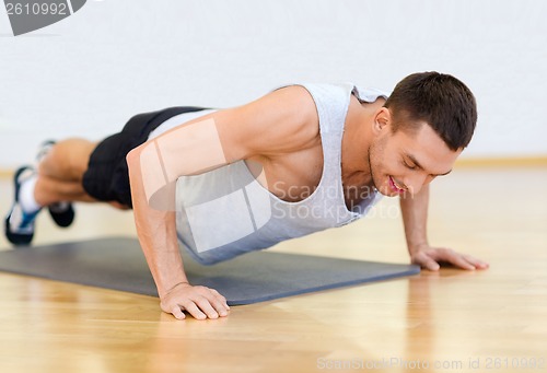 Image of smiling man doing push-ups in the gym