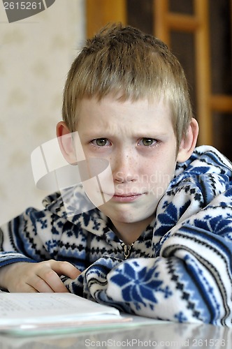 Image of The 10-year-old boy with tears in the eyes sits before the textb