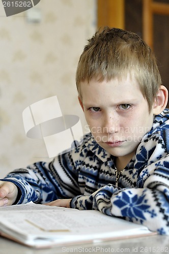 Image of The 10-year-old boy with tears in the eyes sits before the textb