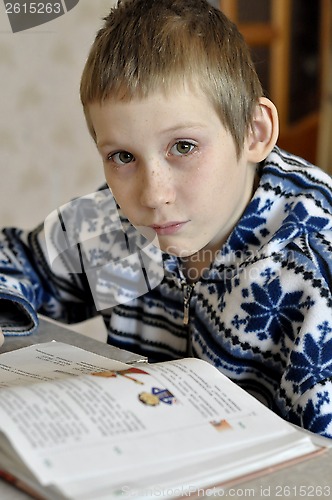 Image of The 10-year-old boy with tears in the eyes sits before the textb