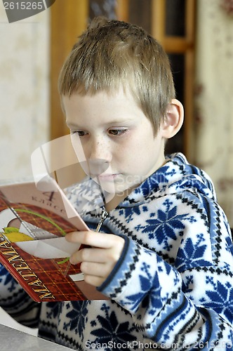 Image of The 10-year-old boy sits with the textbook, doing homework.