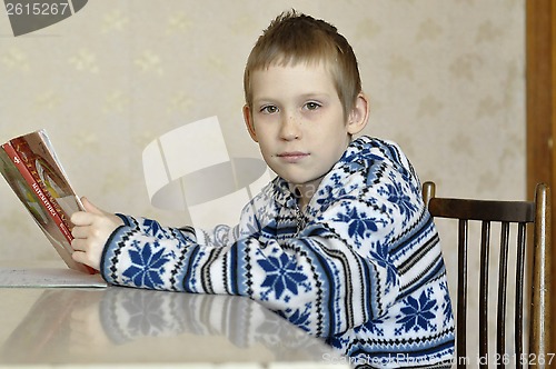 Image of The 10-year-old boy sits with the textbook, doing homework.