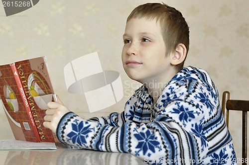 Image of The 10-year-old boy sits with the textbook, doing homework.