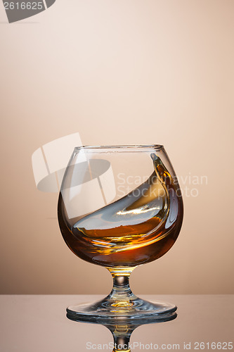 Image of Splash of cognac in glass on brown background