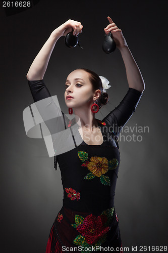 Image of young woman dancing flamenco with castanets on black