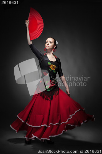 Image of young woman dancing flamenco with fan on black