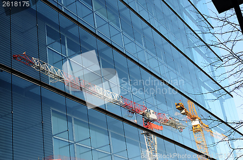 Image of two cranes are reflected in a glass wall of building