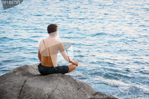 Image of Man sitting in lotus position and looking at the sea