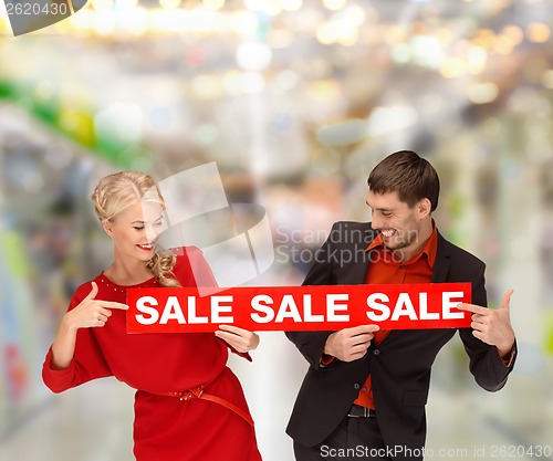 Image of woman and man pointing finger to red sale sign