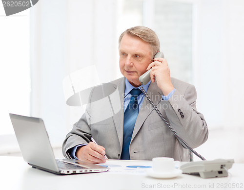 Image of busy older businessman with laptop and telephone