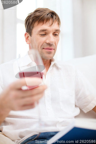 Image of happy man with book and glass of red wine at home