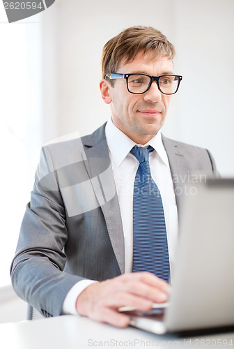Image of businessman in eyeglasses with laptop in office