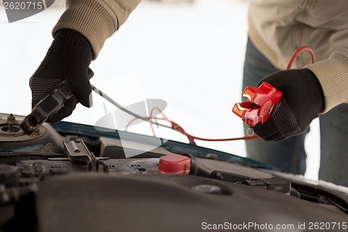 Image of closeup of man under bonnet with starter cables