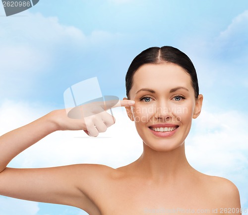 Image of young calm woman pointing to her eye