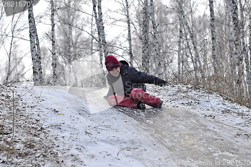 Image of the teenage boy rides from a hill in the snow-covered wood.