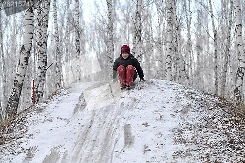 Image of the teenage boy rides from a hill in the snow-covered wood.