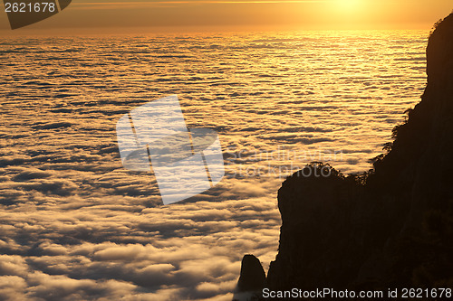 Image of Silhouette of rocks and sea in sunlit clouds at sunset