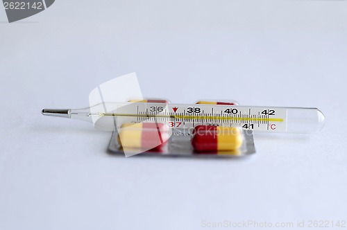 Image of The increased temperature on a thermometer and pills.