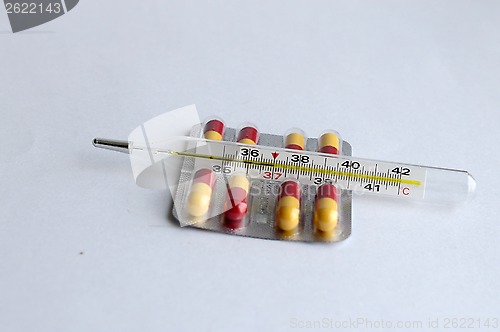 Image of The increased temperature on a thermometer and pills.