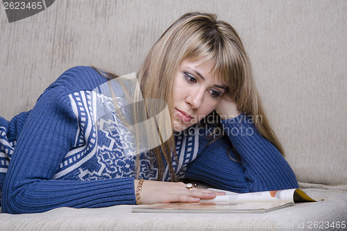 Image of Girl reading book, covered with blanket on couch