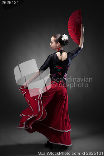 Image of young woman dancing flamenco with fan on black