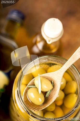 Image of Close up green olives in bank,  bottle of olive oil, rosemary