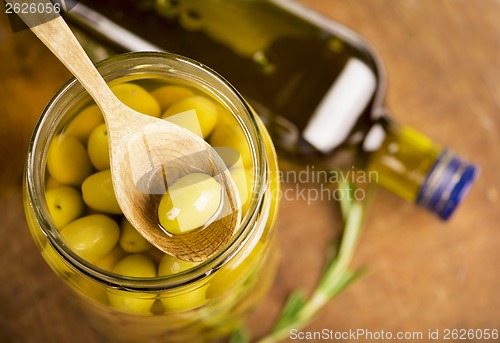 Image of Close up green olives in bank,  bottle of olive oil, rosemary