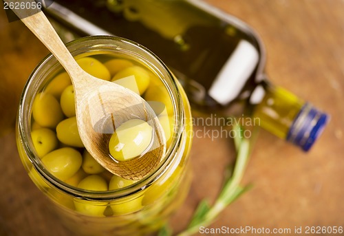 Image of Close up green olives in bank,  bottle of olive oil, rosemary