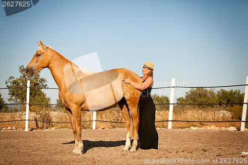 Image of young woman training horse outside in summer