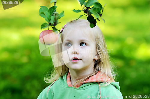 Image of little girl thoughtfully looks at the apple 