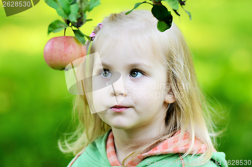 Image of little girl thoughtfully looks at the apple in garden