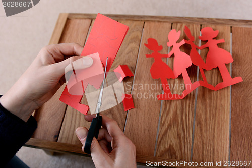 Image of Cutting a chain of red paper dolls with scissors