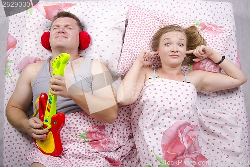 Image of husband plays guitar, wife covered her fingers in his ears