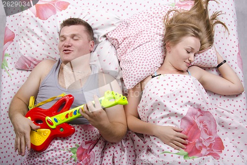 Image of husband plays  guitar, the wife sleeps