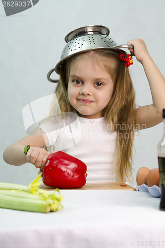 Image of Girl playing in cook put a colander on his head