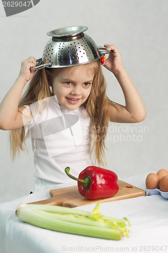 Image of Girl playing in cook put a colander on his head