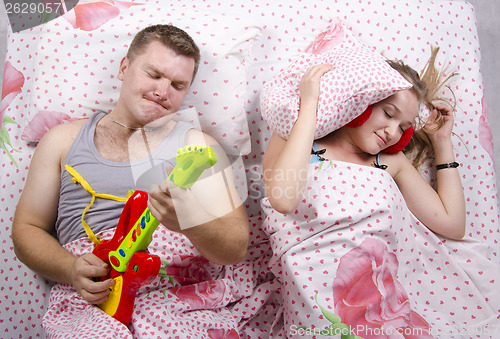 Image of husband plays guitar, wife covered her pillow