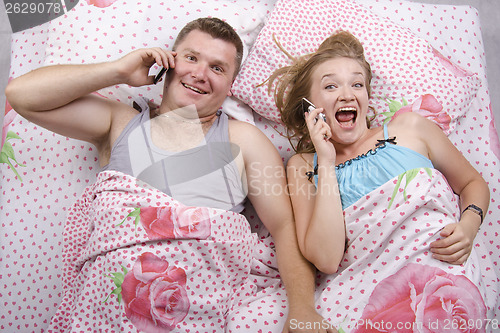 Image of Young couple talking on the phone lying in bed