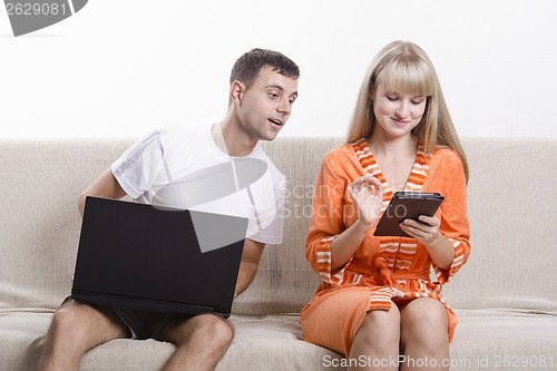 Image of guy with laptop sitting on couch, looking at tablet girl