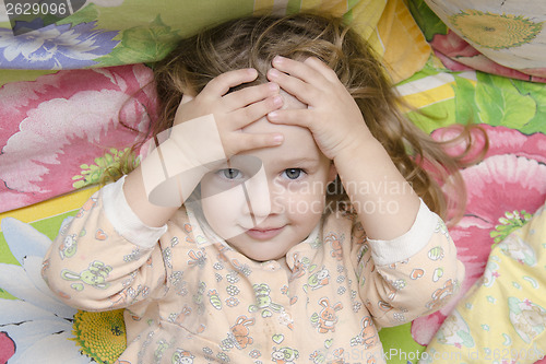 Image of Two-year-old girl lying on bed and head in his hands