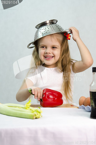 Image of Girl playing in cook put a colander on his head