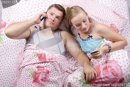 Image of Young couple talking on the phone lying in bed