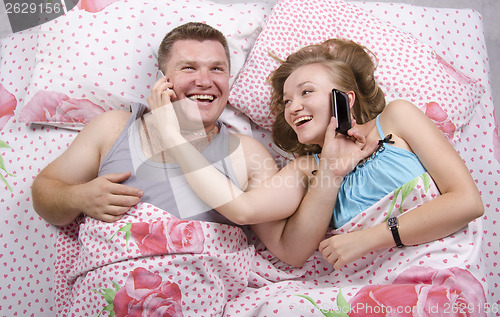 Image of Young couple talking on the phone lying in bed