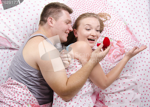 Image of young man gives a ring girl lying in bed