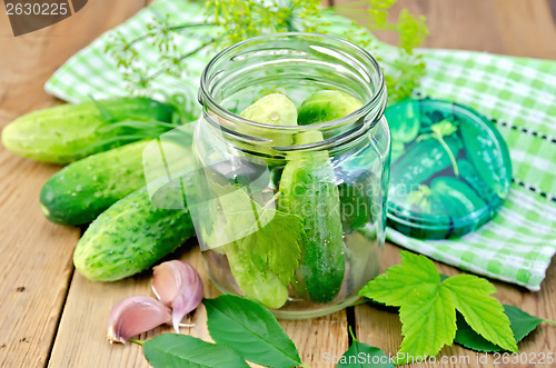 Image of Cucumbers in jar with leaves and napkin on the board